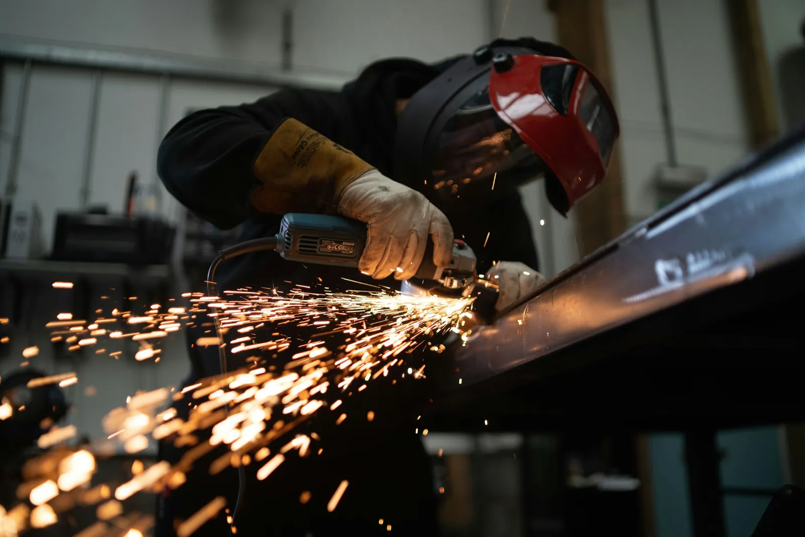 A person in a welding helmet grinds a steel beam as sparks fly