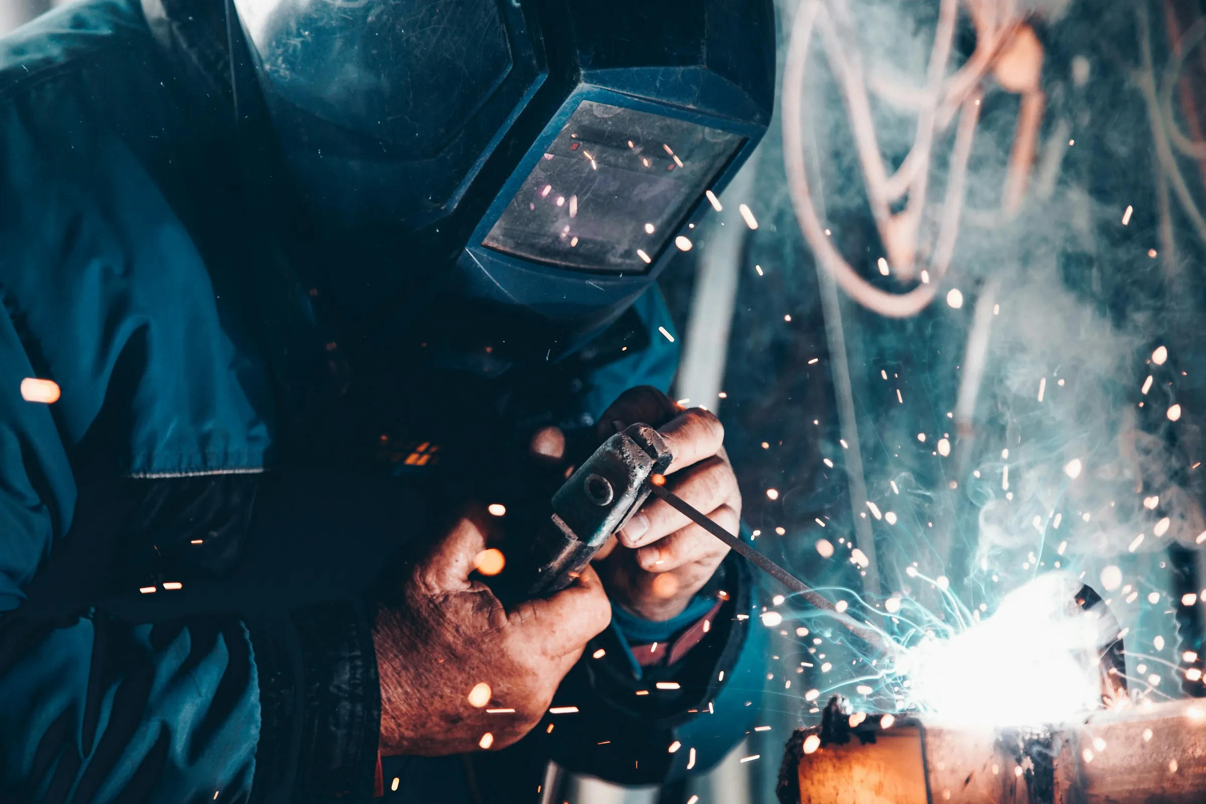 A welder in a mask works with a stick welder as sparks fly